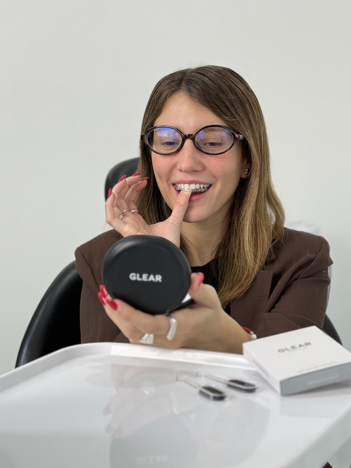Una mujer se coloca el alineador frente al espejo de su estuche GLEAR, sonriendo