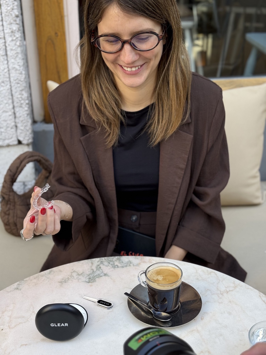 Una mujer sostiene su alineador en la mano, junto a un café y el estuche GLEAR