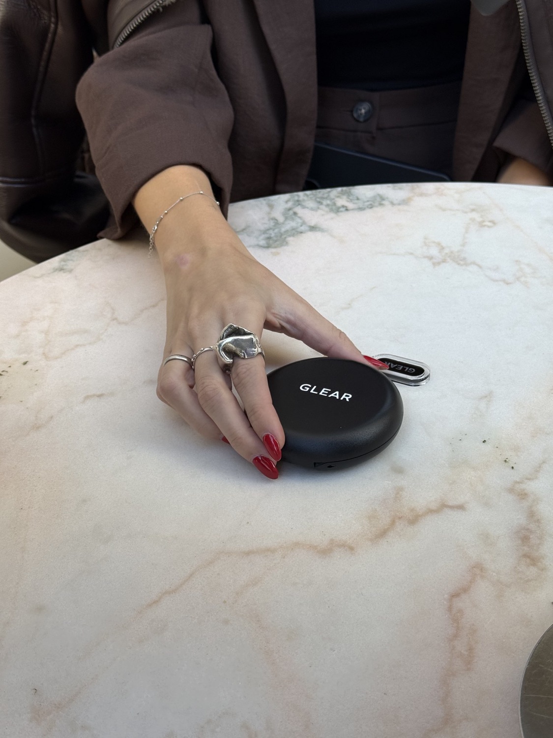 Una mano apoyada sobre el estuche GLEAR en una mesa de mármol